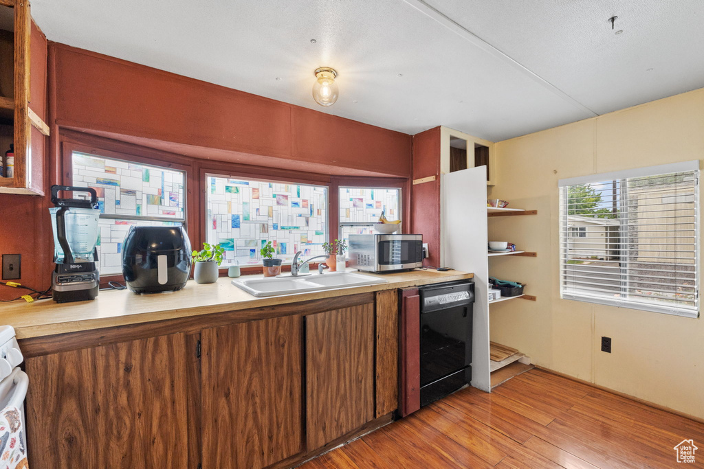 Kitchen featuring black dishwasher, sink, light wood-type flooring, and range