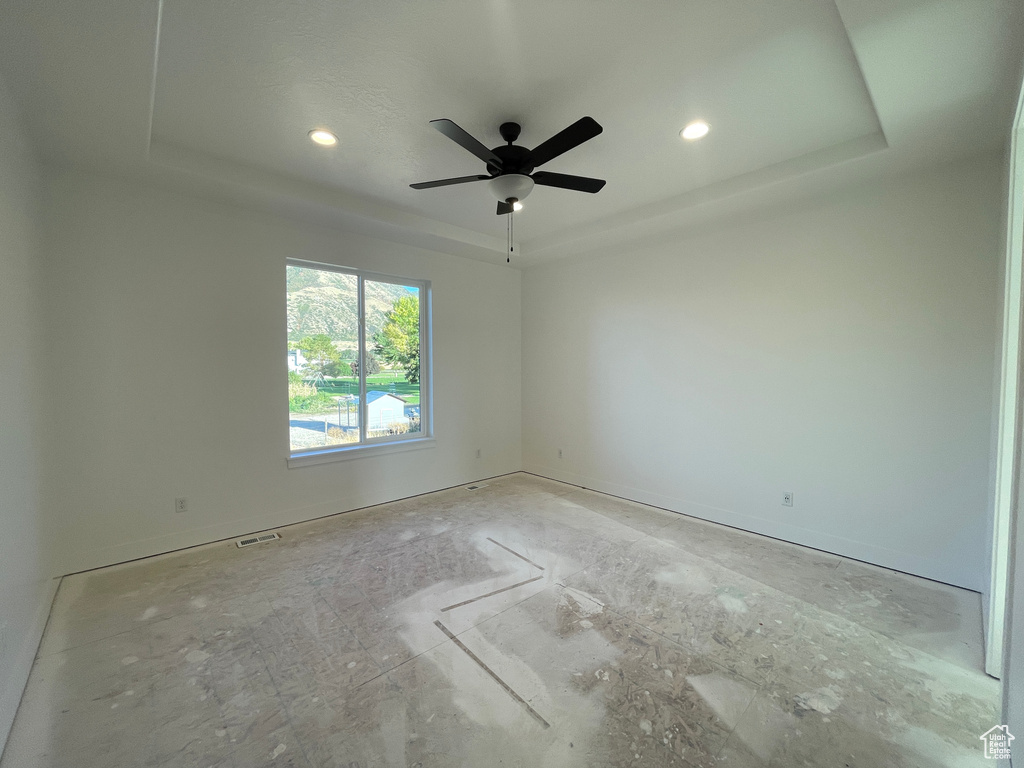 Unfurnished room with ceiling fan and a tray ceiling