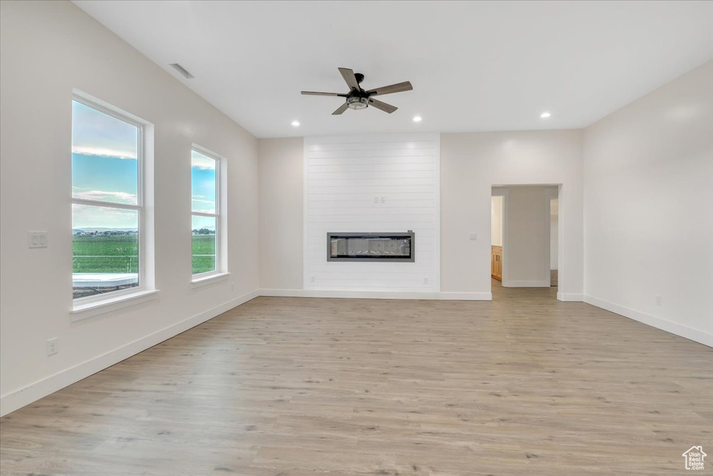 Unfurnished living room with brick wall, light hardwood / wood-style floors, a fireplace, and ceiling fan