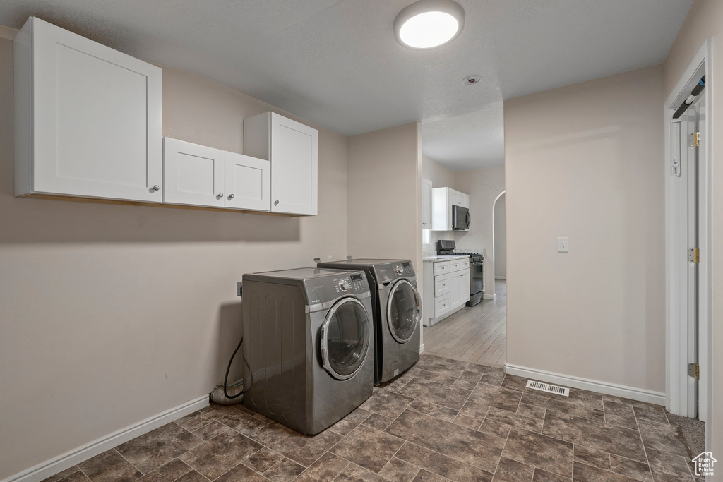 Washroom featuring cabinets, dark tile flooring, and washing machine and clothes dryer