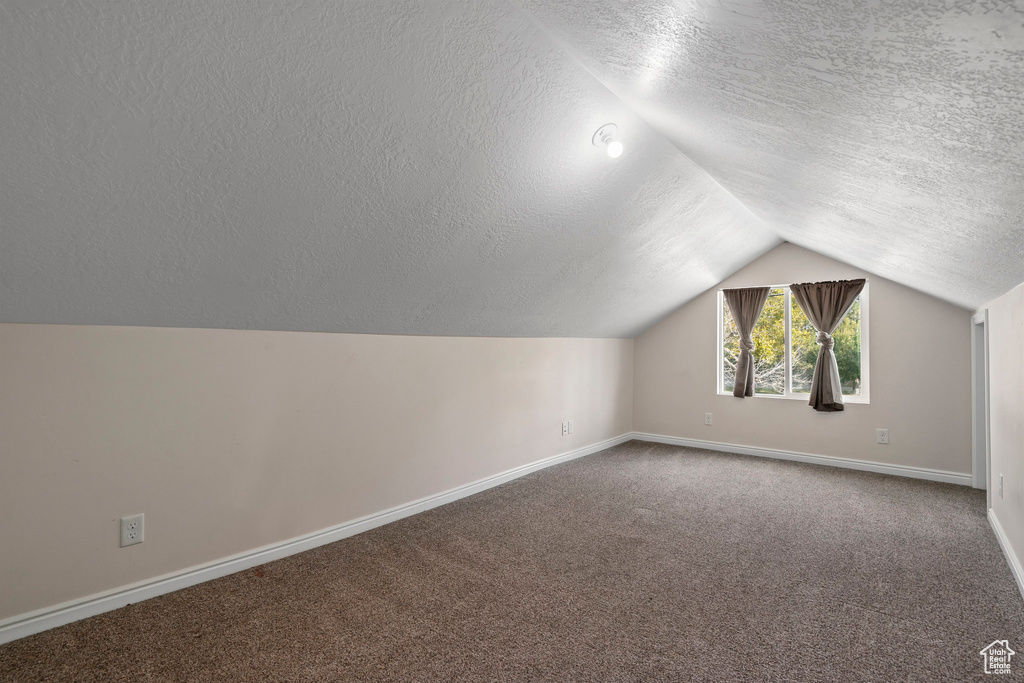 Bonus room featuring lofted ceiling, carpet flooring, and a textured ceiling