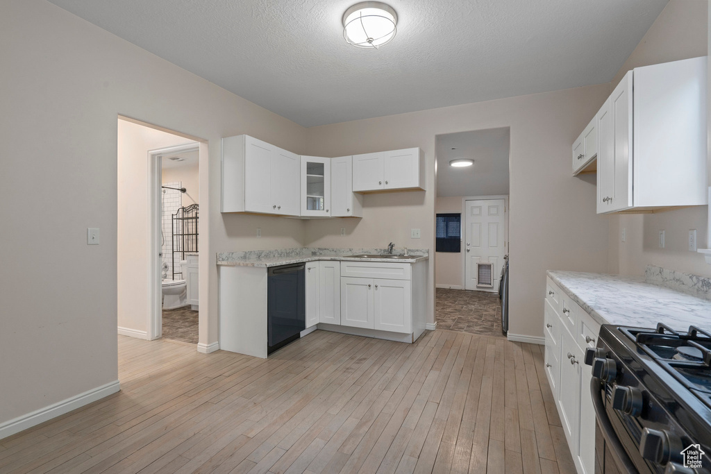 Kitchen featuring sink, light hardwood / wood-style floors, black dishwasher, white cabinets, and stainless steel gas range