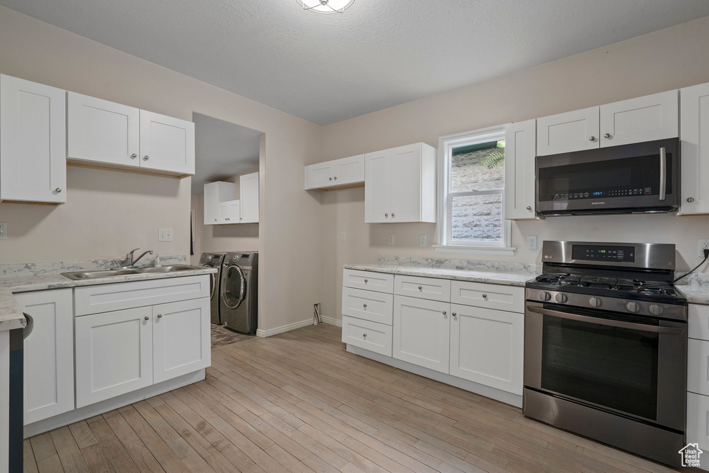 Kitchen with light wood-type flooring, white cabinetry, appliances with stainless steel finishes, washing machine and clothes dryer, and sink