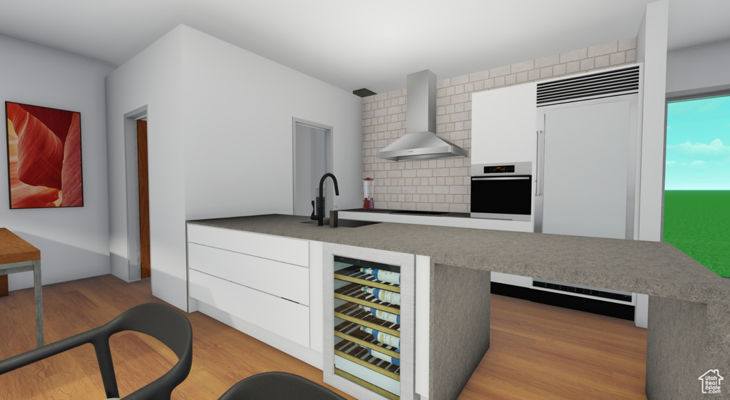 Kitchen with wall chimney range hood, light wood-type flooring, white cabinets, tasteful backsplash, and stainless steel oven