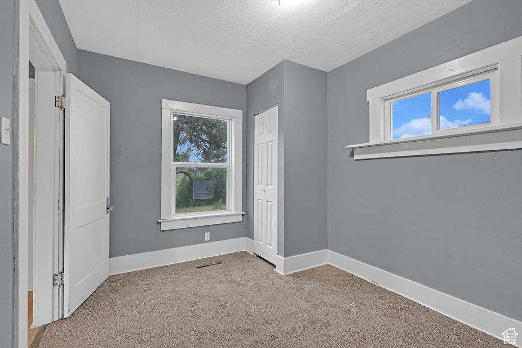 Unfurnished bedroom with light carpet, a closet, and a textured ceiling