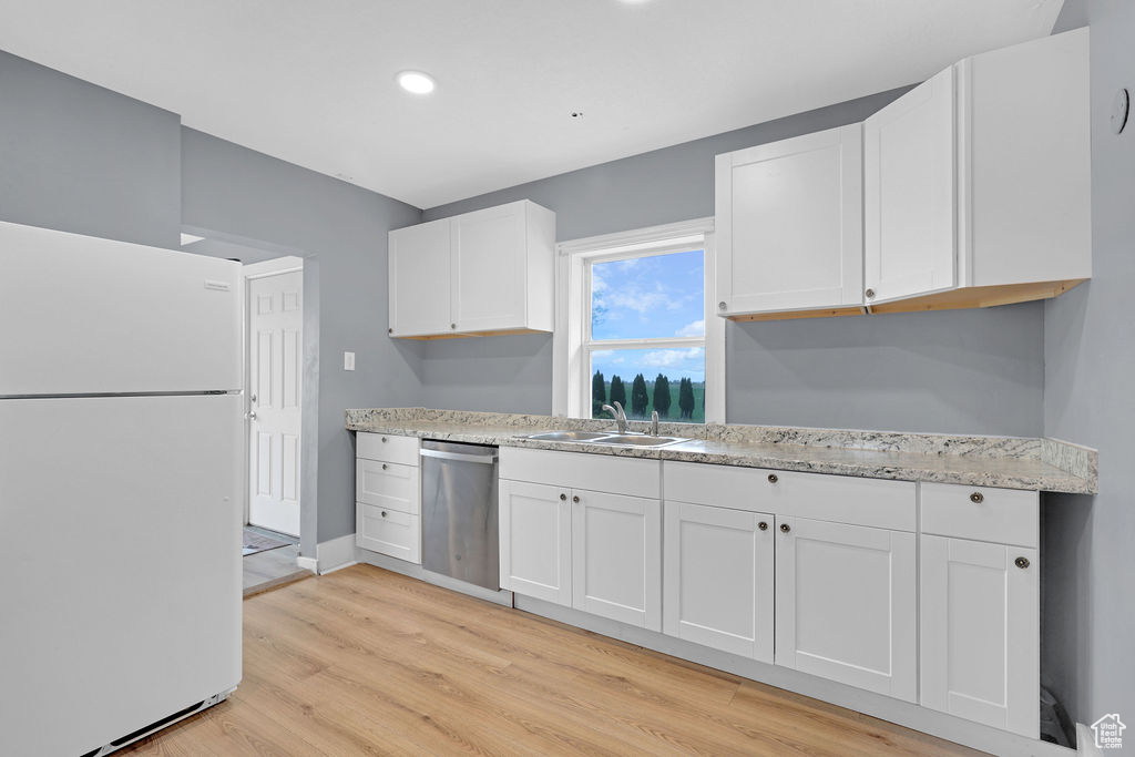 Kitchen with stainless steel dishwasher, white refrigerator, light wood-type flooring, sink, and white cabinetry