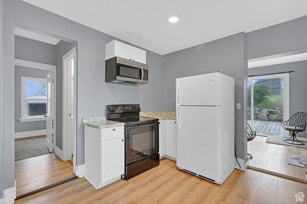 Kitchen featuring white cabinets, black range with electric cooktop, white fridge, and light hardwood / wood-style flooring