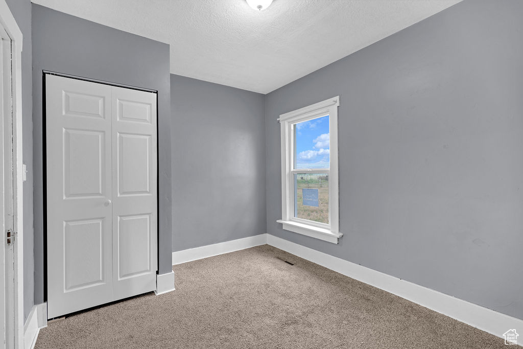 Unfurnished bedroom with a textured ceiling, a closet, and carpet