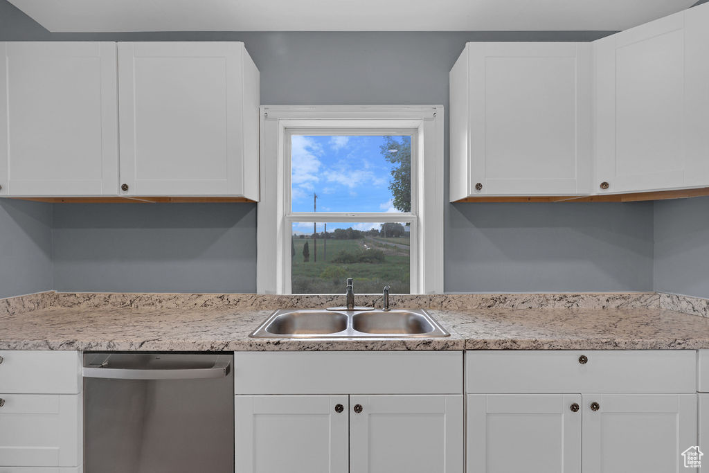 Kitchen with sink, white cabinets, light stone countertops, and stainless steel dishwasher