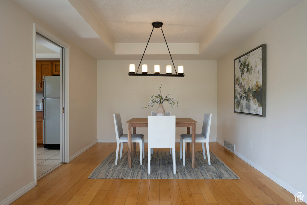 Unfurnished dining area featuring light hardwood / wood-style floors, an inviting chandelier, and a raised ceiling