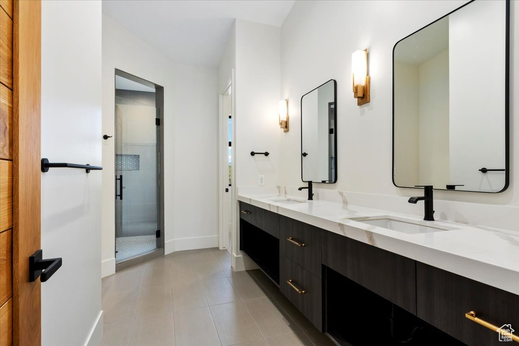 Bathroom with a shower with shower door, tile flooring, double sink, and vanity with extensive cabinet space