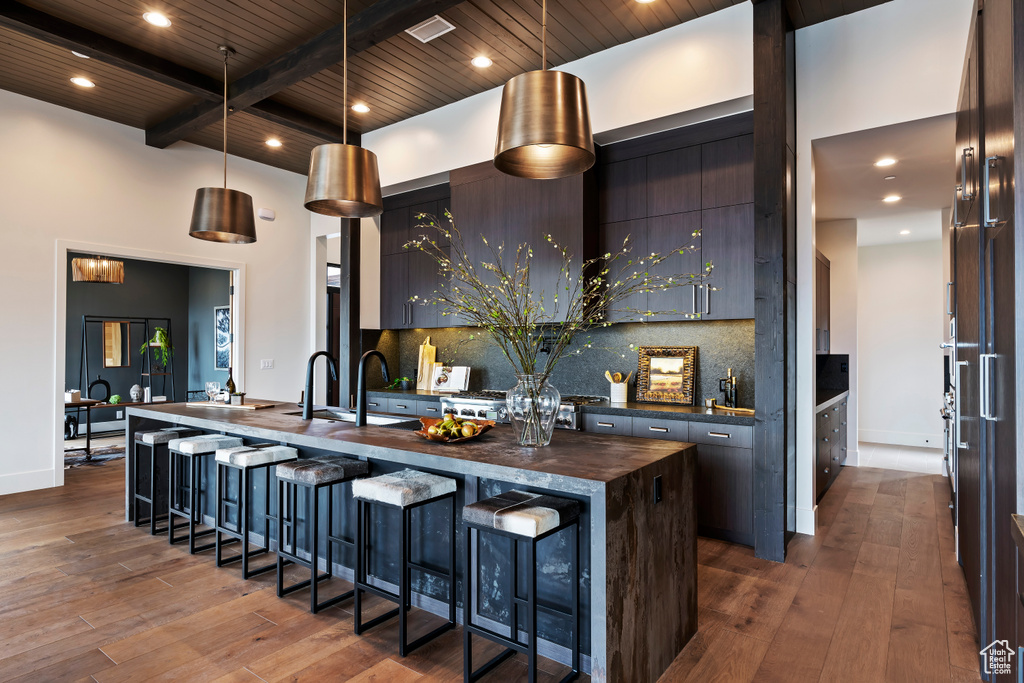 Kitchen with tasteful backsplash, a center island with sink, beamed ceiling, pendant lighting, and dark wood-type flooring