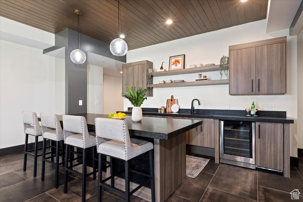 Kitchen featuring hanging light fixtures, a center island, a breakfast bar area, wine cooler, and dark tile patterned flooring