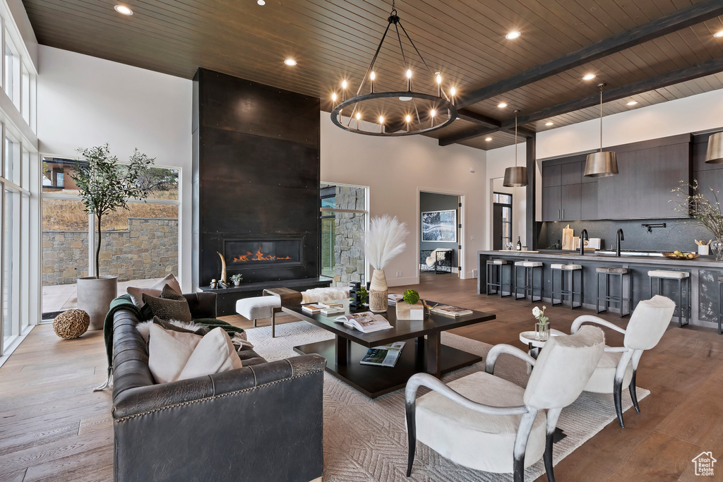 Living room with a large fireplace, a high ceiling, light wood-type flooring, a chandelier, and wooden ceiling