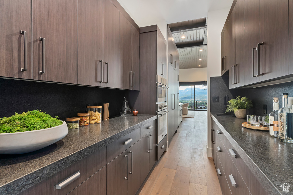 Kitchen with light hardwood / wood-style flooring, decorative backsplash, oven, and dark brown cabinetry