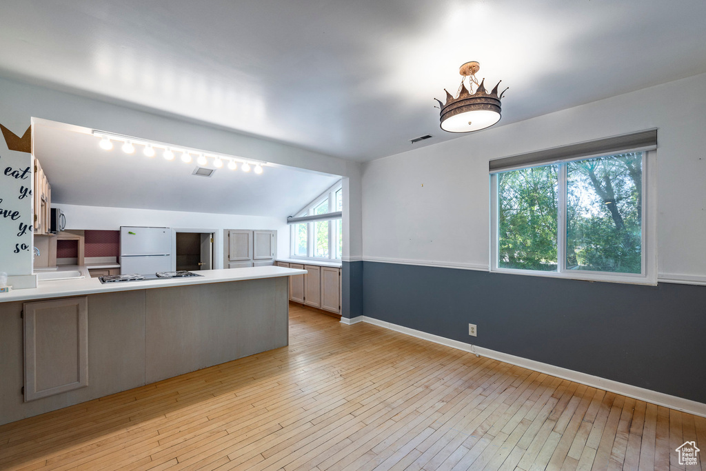 Kitchen with white refrigerator, vaulted ceiling, light hardwood / wood-style flooring, and stainless steel gas cooktop