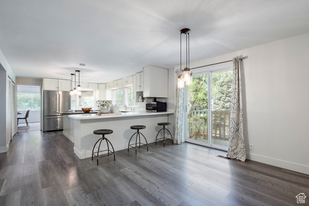 Kitchen with white cabinetry, dark hardwood / wood-style floors, stainless steel refrigerator, and kitchen peninsula