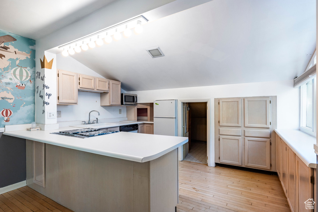 Kitchen featuring vaulted ceiling, light brown cabinetry, light hardwood / wood-style flooring, kitchen peninsula, and sink