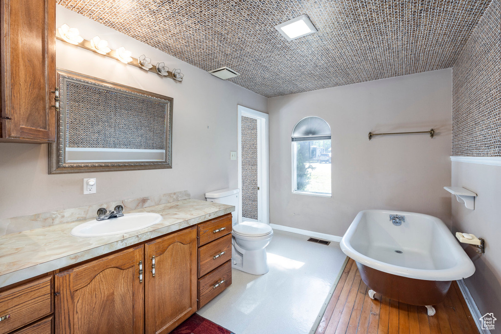 Bathroom with wood-type flooring, large vanity, a washtub, and toilet