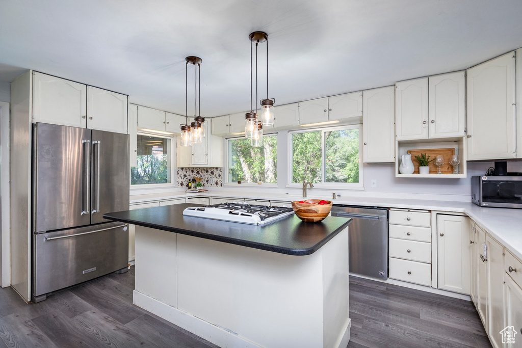 Kitchen featuring dark wood-type flooring, hanging light fixtures, a center island, white cabinets, and appliances with stainless steel finishes