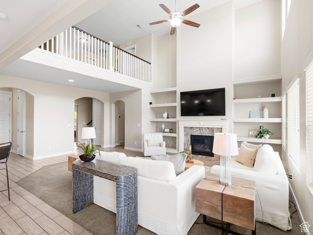 Living room featuring a premium fireplace, a high ceiling, ceiling fan, and a healthy amount of sunlight