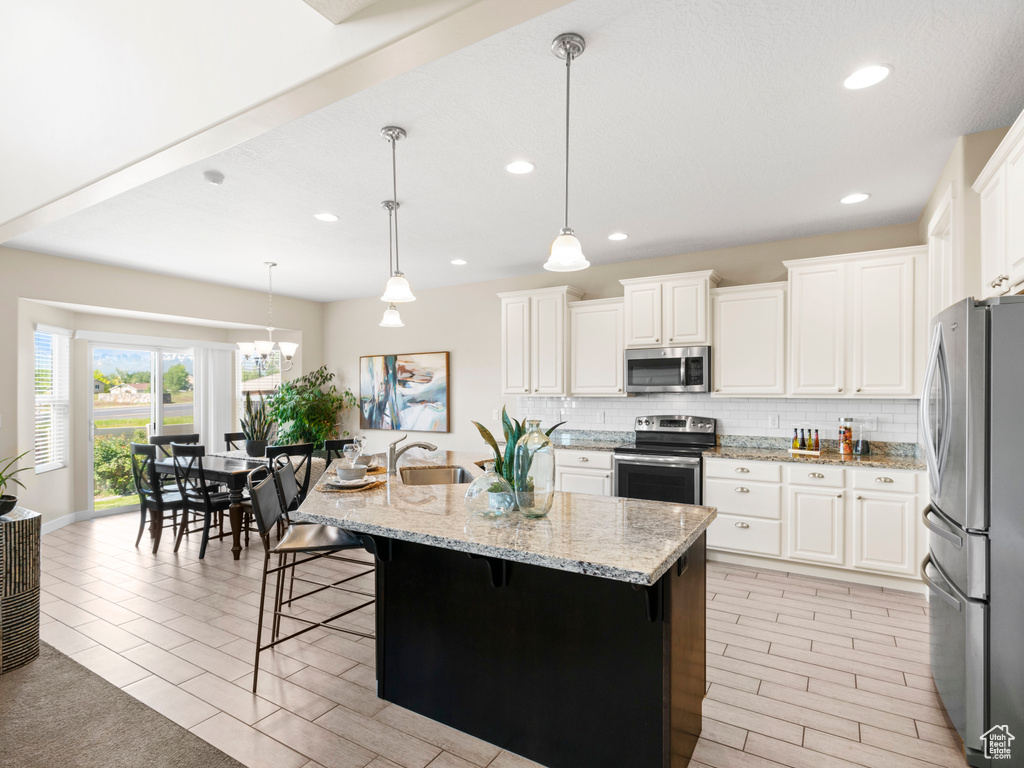 Kitchen featuring a center island with sink, tasteful backsplash, appliances with stainless steel finishes, a breakfast bar, and pendant lighting