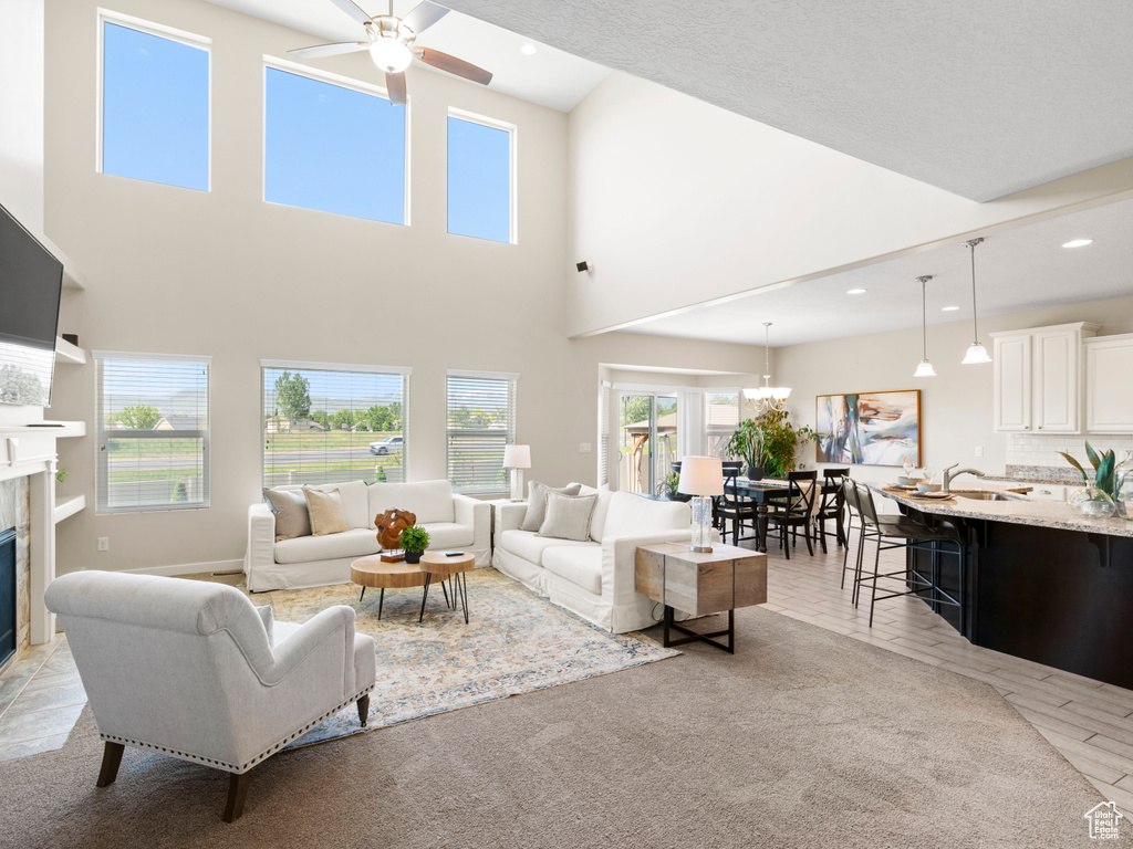 Living room with a high ceiling, a premium fireplace, ceiling fan with notable chandelier, and sink