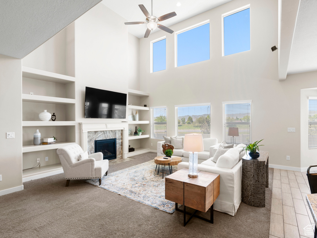 Living room with a premium fireplace, a towering ceiling, ceiling fan, and built in shelves