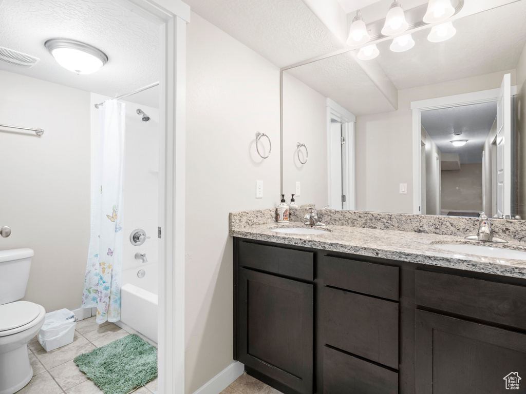 Full bathroom with tile floors, double vanity, toilet, and shower / bath combo with shower curtain