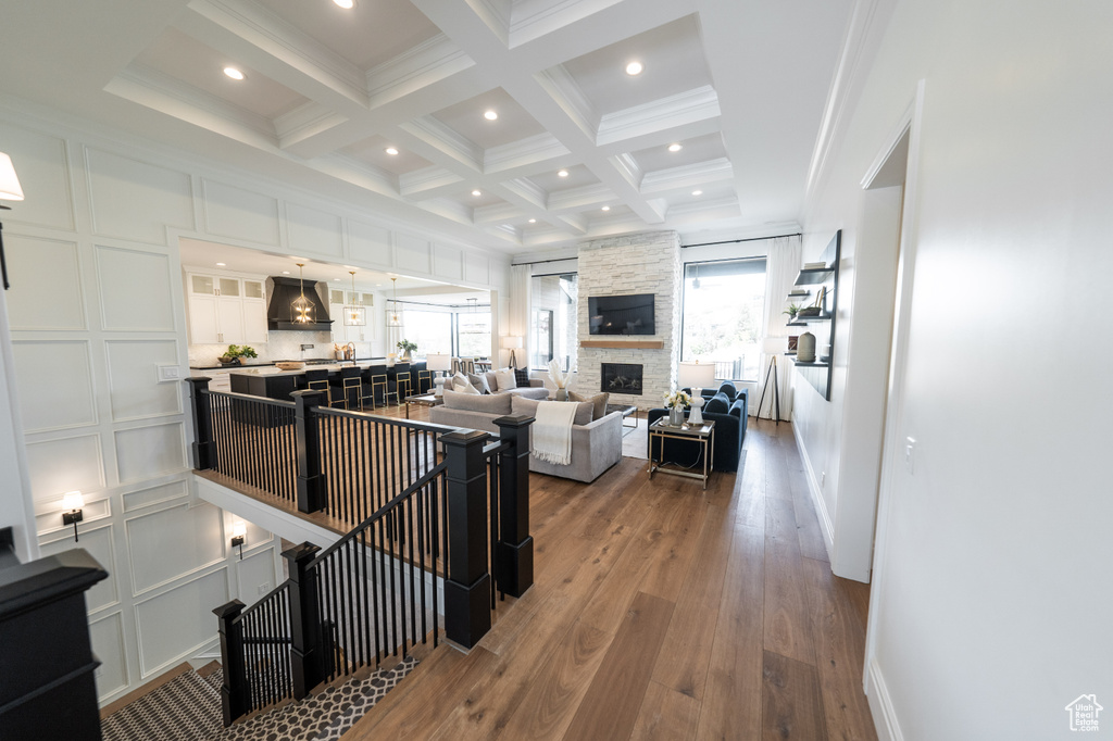 Interior space with a stone fireplace, hardwood / wood-style floors, beamed ceiling, coffered ceiling, and ornamental molding