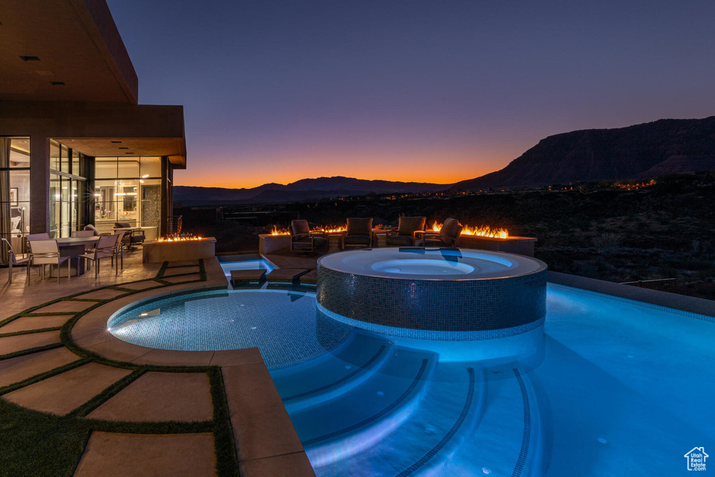 Pool at dusk with an in ground hot tub, a mountain view, and a patio area