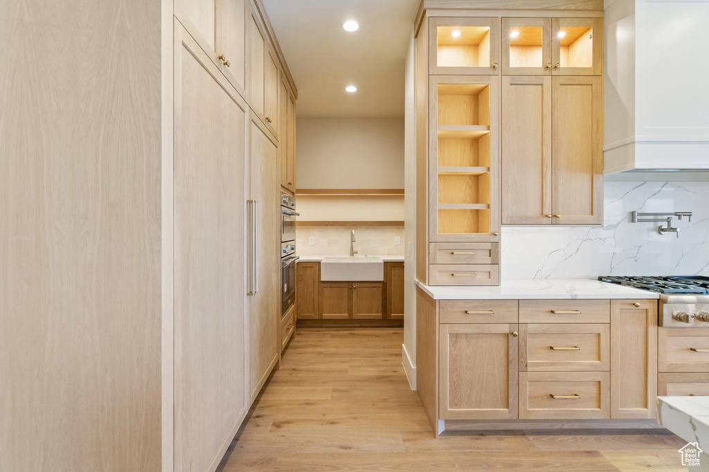 Kitchen with light brown cabinetry, sink, tasteful backsplash, and light hardwood / wood-style floors