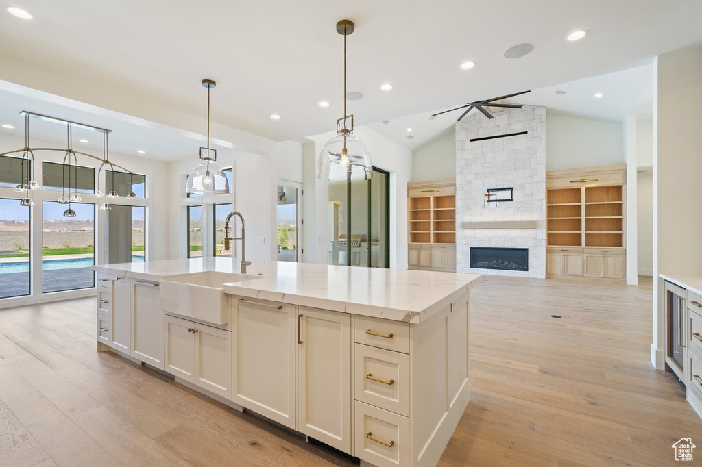 Kitchen with vaulted ceiling, light stone countertops, a fireplace, an island with sink, and sink