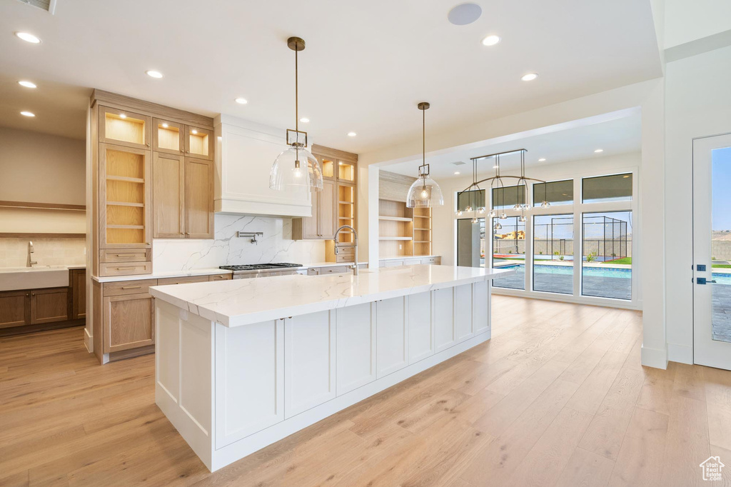 Kitchen featuring light wood-type flooring, hanging light fixtures, a large island, and light stone counters