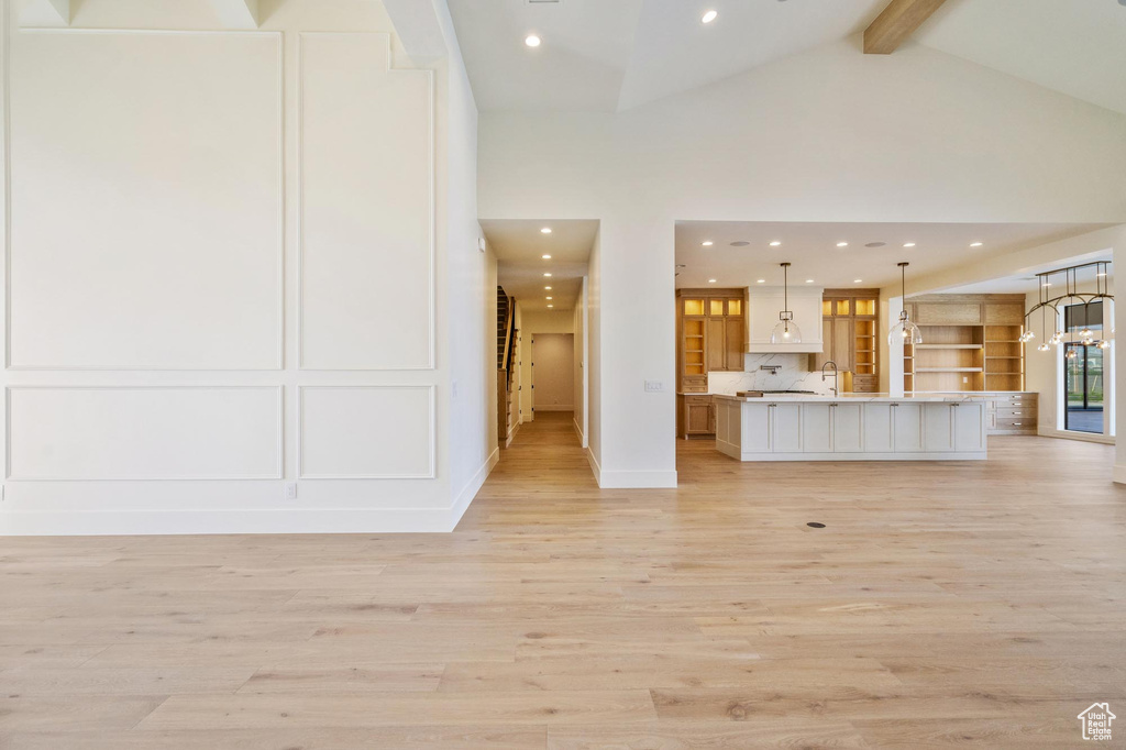 Unfurnished living room with light wood-type flooring, beamed ceiling, and high vaulted ceiling