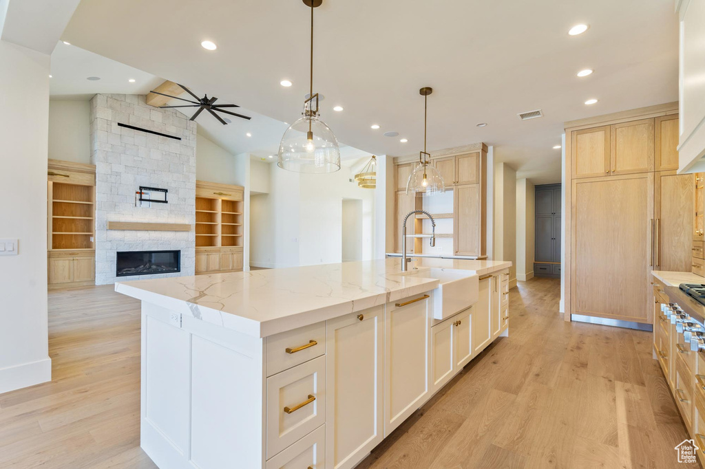 Kitchen featuring a kitchen island with sink, sink, ceiling fan, a stone fireplace, and lofted ceiling