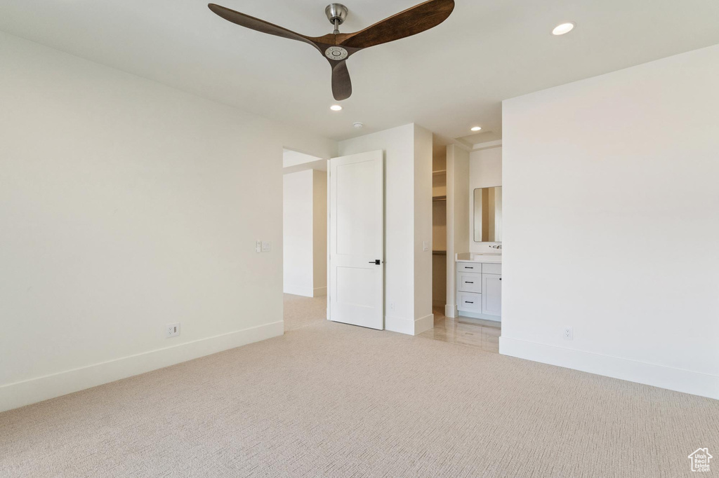 Unfurnished bedroom with ensuite bath, light colored carpet, a spacious closet, and ceiling fan