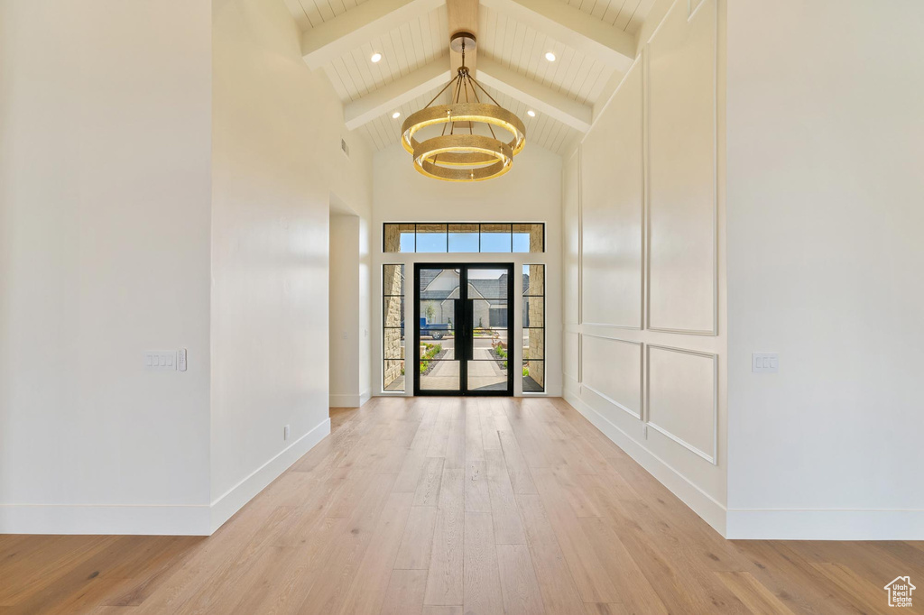 Unfurnished room with beamed ceiling, high vaulted ceiling, an inviting chandelier, and light hardwood / wood-style floors