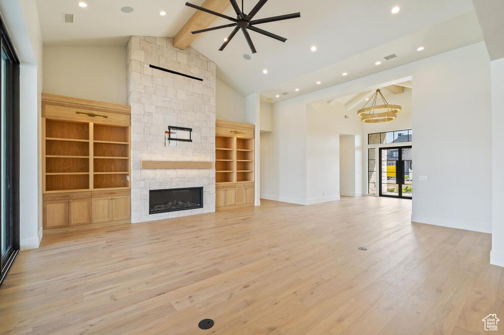 Unfurnished living room featuring light hardwood / wood-style flooring, ceiling fan with notable chandelier, beamed ceiling, a stone fireplace, and high vaulted ceiling