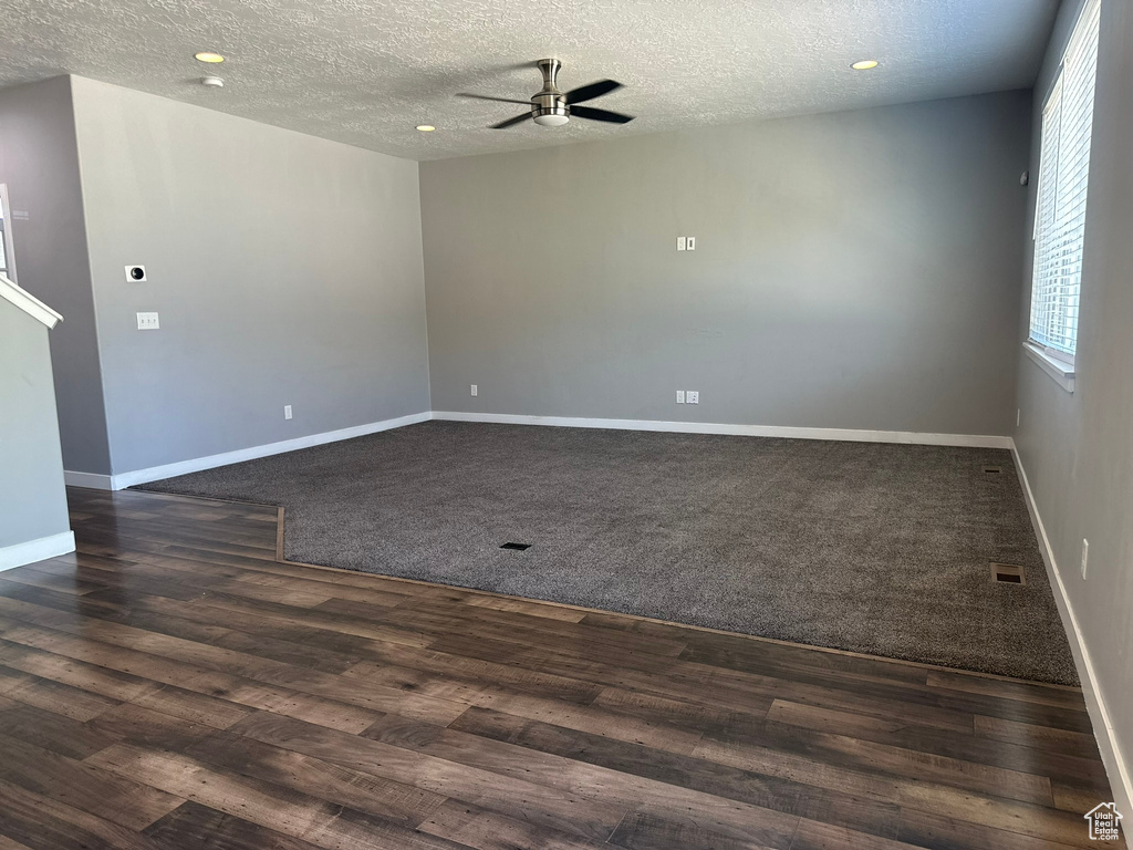Empty room with ceiling fan, dark colored carpet, and a textured ceiling