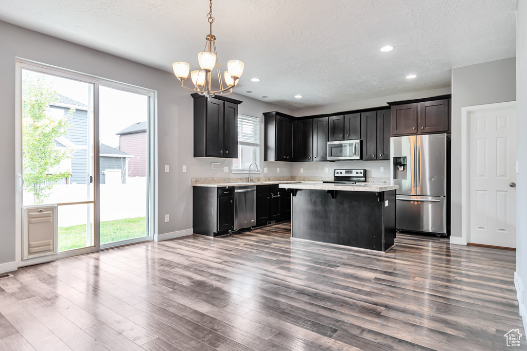 Kitchen with hardwood / wood-style flooring, decorative light fixtures, a kitchen island, a wealth of natural light, and appliances with stainless steel finishes