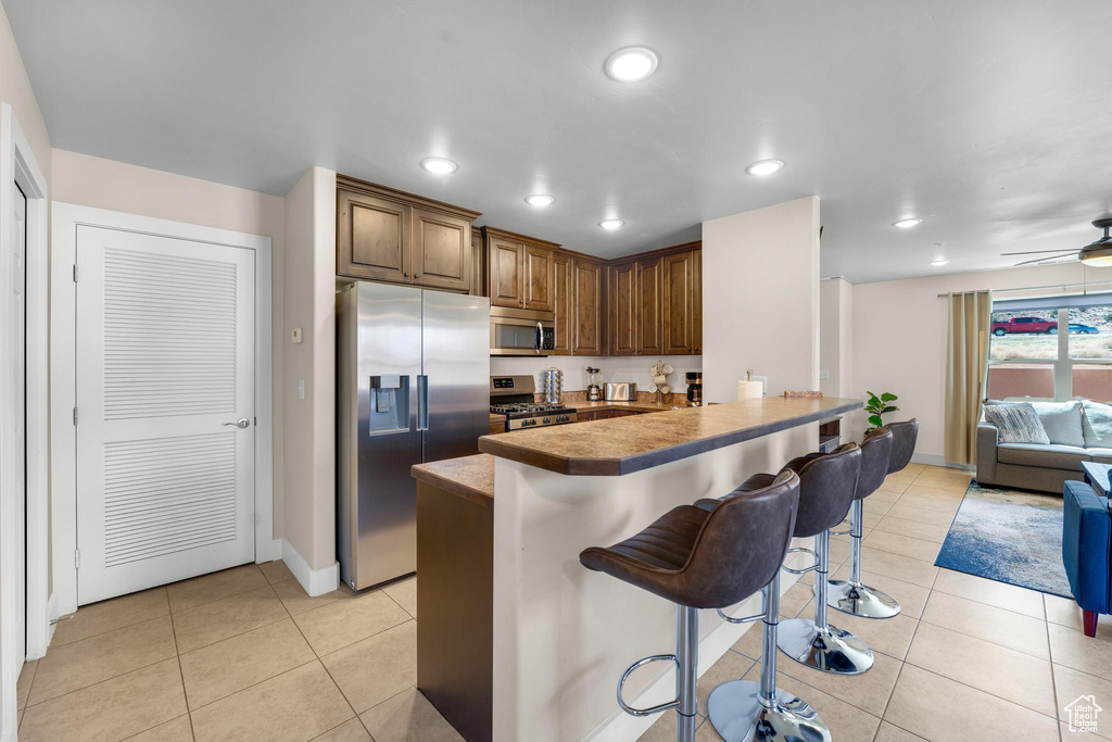 Kitchen with stainless steel appliances, kitchen peninsula, light tile flooring, ceiling fan, and a kitchen bar