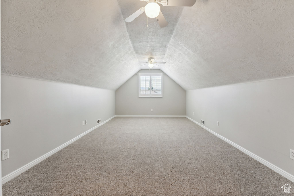 Additional living space with ceiling fan, vaulted ceiling, a textured ceiling, and carpet flooring