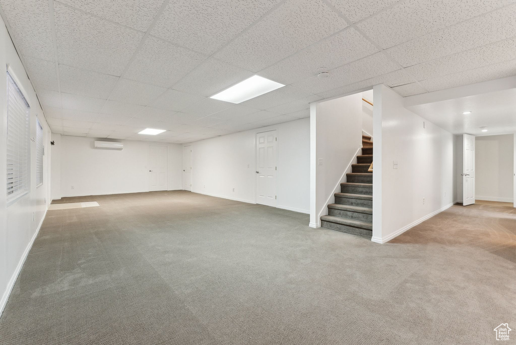 Basement featuring a wall mounted air conditioner, carpet, and a drop ceiling