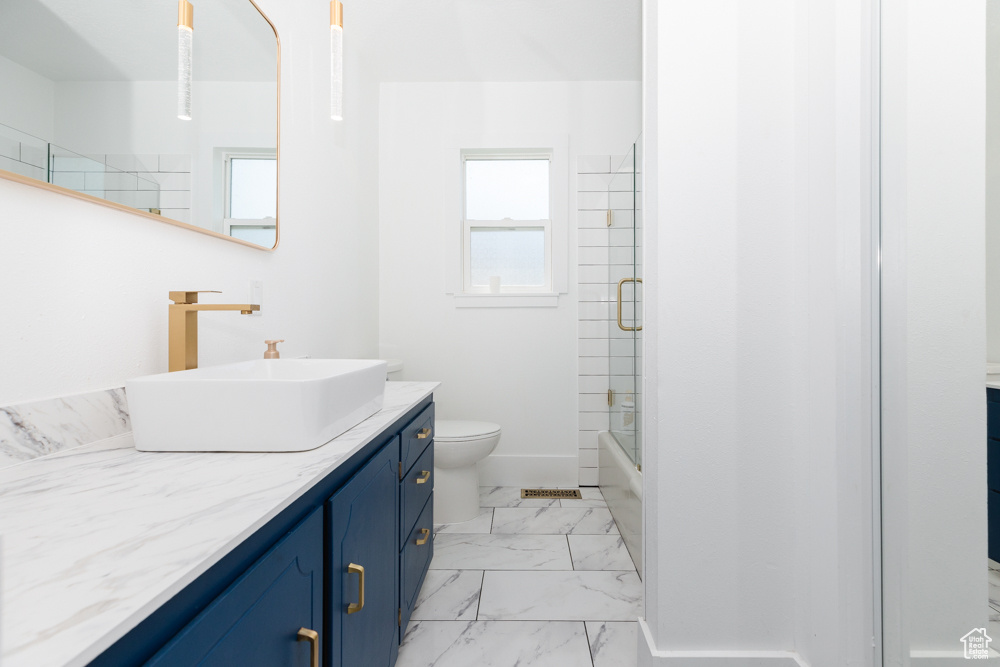 Full bathroom with tile floors, bath / shower combo with glass door, toilet, and vanity