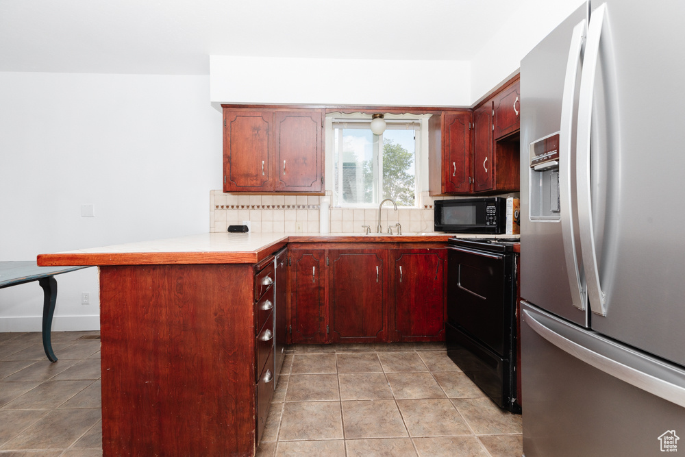 Kitchen featuring kitchen peninsula, black appliances, backsplash, light tile floors, and sink