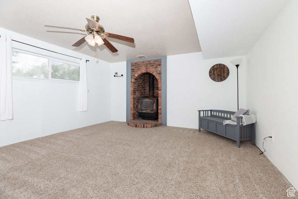 Unfurnished room featuring brick wall, ceiling fan, carpet, and a wood stove