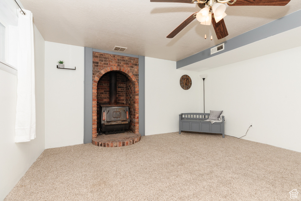 Unfurnished living room with brick wall, carpet flooring, ceiling fan, and a wood stove