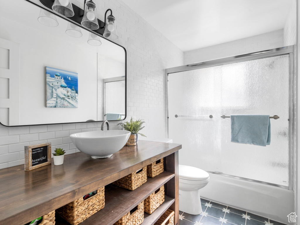 Full bathroom featuring tile walls, toilet, tile floors, bath / shower combo with glass door, and vanity