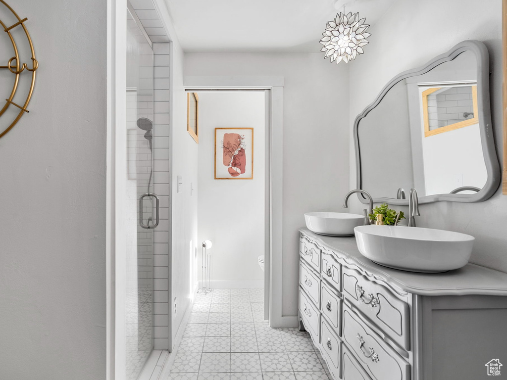 Bathroom with toilet, tile flooring, large vanity, walk in shower, and double sink